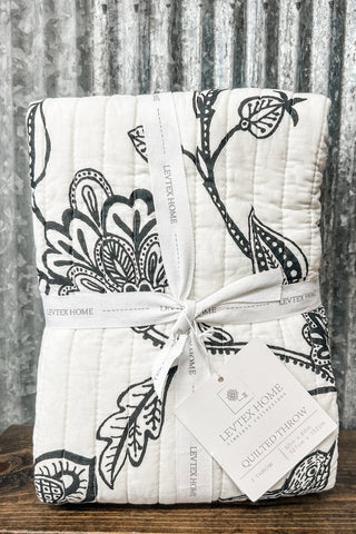 Quilt with black floral patterns on a wooden surface and rustic background